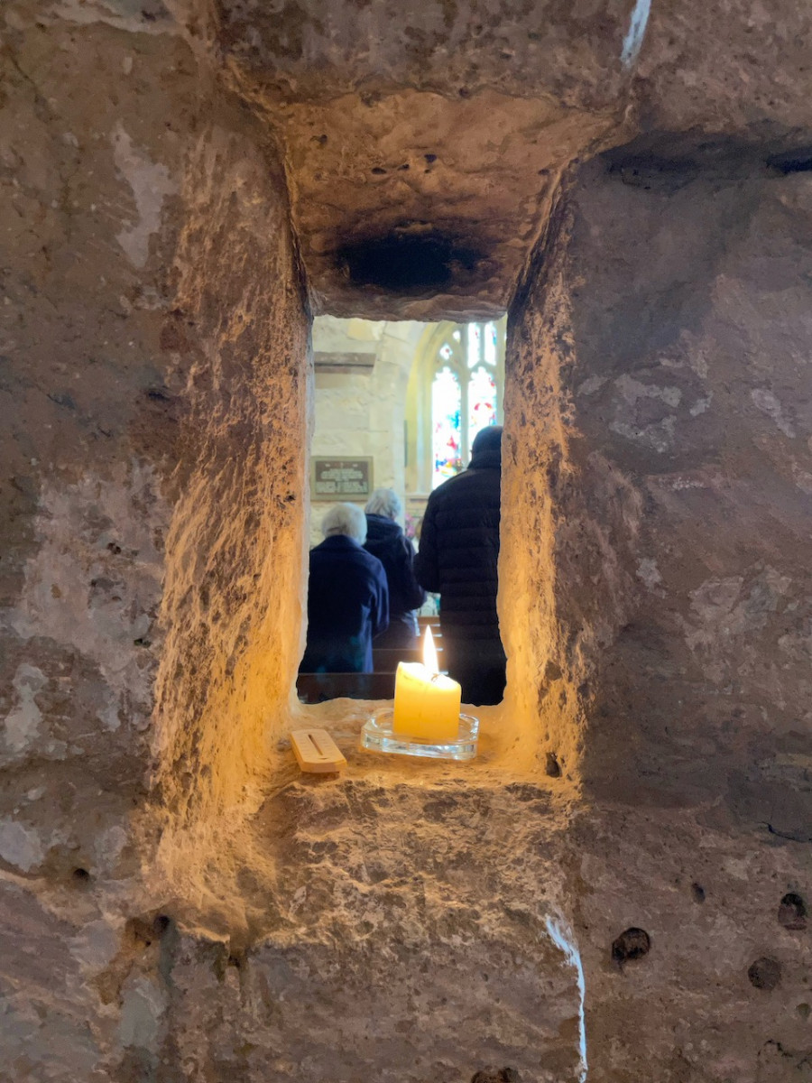 A lit candle sitting in an alcove with people worshipping beyond